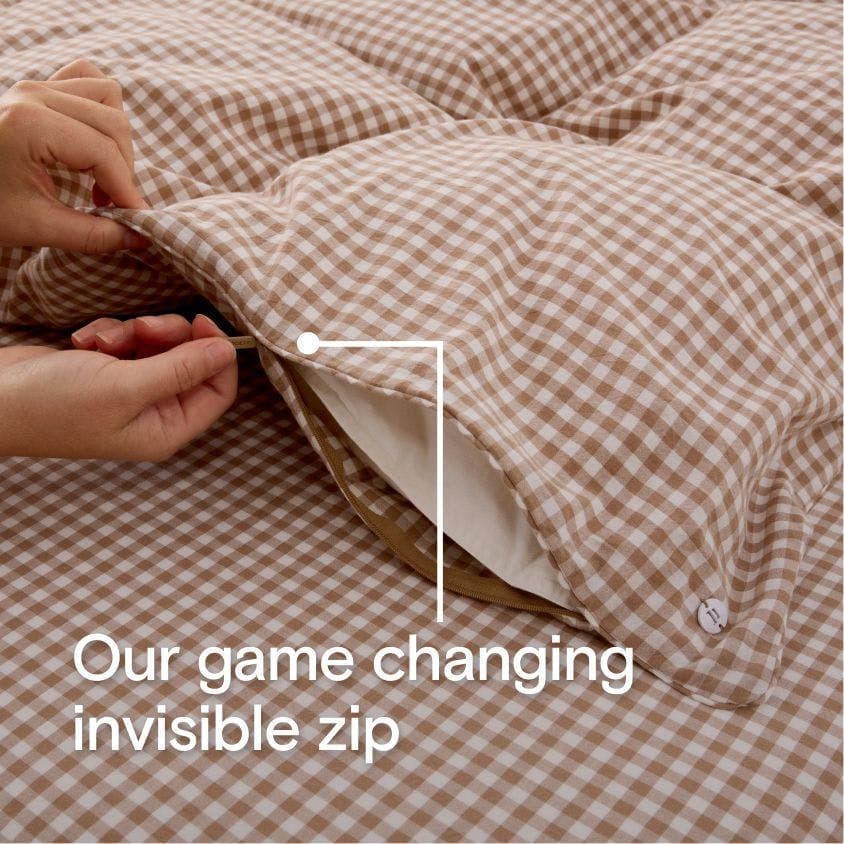 A hand demonstrating the invisible zip of a duvet cover, with overlay text that reads 'Our game changing invisible zip.'